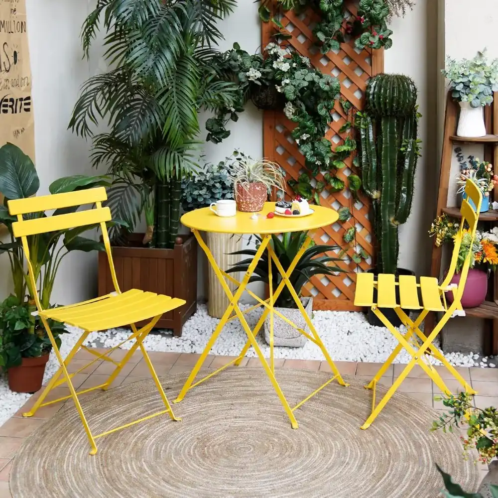 Yellow folding bistro set of a round table and two slatted chairs on a patio with plants